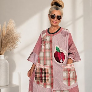 Peut inclure: Robe patchwork aux tons de rouge, blanc et marron, avec des motifs à carreaux et rayés. La robe a de grandes poches et une application de pomme à paillettes. Les manches sont aux trois quarts.