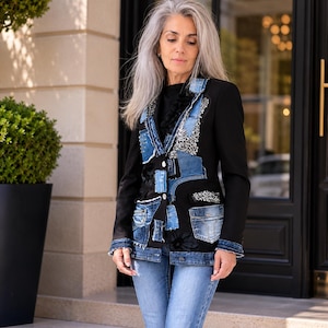 May include: A black blazer with denim patchwork detailing. The jacket features various shades of blue denim patches, pockets, and embellishments. The model is wearing the jacket with blue jeans.