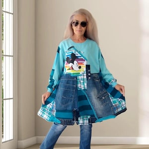 Puede incluir: Una sudadera de manga larga en color azul claro con un gráfico de Mickey Mouse sobre un fondo de arcoíris. La parte inferior está confeccionada con un mosaico de tela de mezclilla azul, rayas horizontales azul oscuro y un patrón de cuadros.