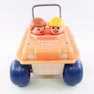 Puede incluir: Un coche de juguete de plástico naranja vintage con ruedas azules. El coche tiene un interior blanco y dice "Bouncing Buggy" en la parte delantera. Dos pequeñas figuras de plástico están sentadas en el coche.