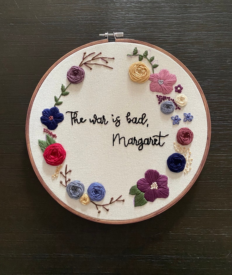 May include: Embroidered hoop art featuring a floral wreath and the text "The war is bad, Margaret".