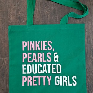 May include: A green canvas tote bag with white and pink lettering that reads "Pinkies, Pearls & Educated Pretty Girls".