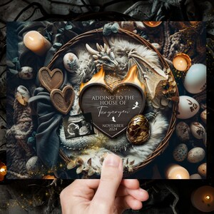 May include: A wooden heart-shaped sign with the text "Adding to the House of Targaryen" and the date "November 2024". The sign is surrounded by a nest of dragon eggs, a dragon figurine, and candles.