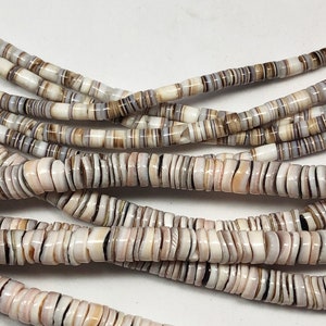 May include: Strands of natural shell beads in varying shades of white, tan, and brown. The beads are small, flat, and disc-shaped, strung together to form necklaces or bracelets. The beads have a natural, organic appearance.
