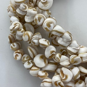 May include: Close-up of a strand of beads. The beads are a mix of white and tan, with a swirled pattern. The beads are smooth and rounded, and appear to be made of a natural material. The beads are strung together, forming a necklace or bracelet.