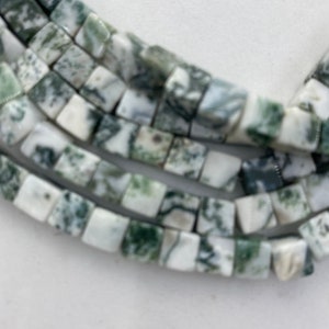May include: Close-up of strands of square-shaped beads. The beads are a mix of white and green, with a mottled pattern. The beads are strung together, creating a necklace or bracelet.