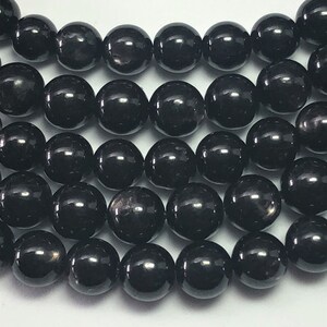 May include: Close-up of a strand of black, glossy, round beads. The beads are evenly sized and reflect light, creating a shiny appearance. The beads are likely used for jewelry making or crafting.