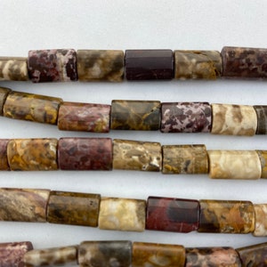May include: Close-up of several strands of rectangular beads. The beads display a mix of colors, including brown, tan, burgundy, and cream. The beads have a polished finish and are strung together, creating a textured and earthy appearance.