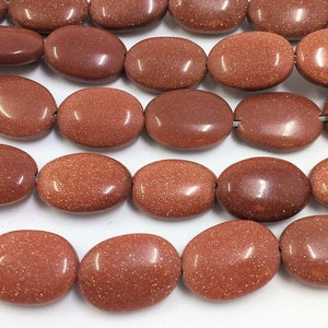 May include: Rows of polished, oval-shaped beads in a warm, reddish-brown hue. The beads have a speckled, glittery appearance, suggesting a metallic or mineral composition. The beads are strung together, ready for jewelry making or crafting.