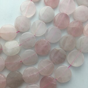 May include: A collection of rose quartz gemstone beads. The beads are flat, round, and vary in shades of pink, from pale to medium. Each bead is strung on a thin, pink thread, suggesting they are for jewelry making.