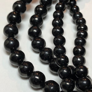 May include: Close-up of multiple strands of glossy, black beads. The beads are round and evenly sized, reflecting light. The image highlights the texture and sheen of the jewelry, suggesting a necklace or bracelet.
