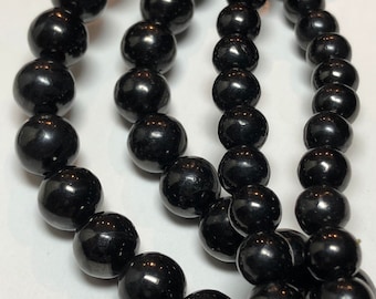 May include: Close-up of multiple strands of glossy, black beads. The beads are round and evenly sized, reflecting light. The image highlights the texture and sheen of the jewelry, suggesting a necklace or bracelet.