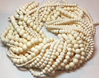 May include: Cream-colored round beads of varying sizes strung together, forming multiple strands. The beads are tightly packed, creating a dense, textured appearance. The beads are likely for jewelry making or crafting.