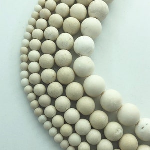 May include: Close-up of a collection of off-white, round beads of varying sizes. The beads are arranged in curved rows, showcasing their spherical shape and subtle color variations. The beads appear to be made of a natural material.