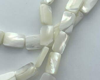 May include: Close-up of a necklace made of rectangular, iridescent, off-white beads. The beads are strung together, creating a delicate and elegant design. The beads have a subtle sheen, reflecting light.