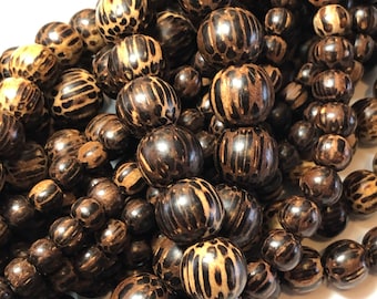 May include: Close-up of a collection of wooden beads in various sizes. The beads have a dark brown base color with lighter brown patterns, some resembling animal prints. The beads are strung together, suggesting they are for jewelry making or crafts.