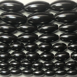 Peut inclure: Gros plan sur des rang&eacute;es de perles noires ovales et brillantes. Chaque perle pr&eacute;sente une surface r&eacute;fl&eacute;chissante avec une fine rayure claire. Les perles sont enfil&eacute;es, probablement pour la cr&eacute;ation de bijoux ou d'artisanat.