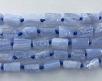 May include: Close-up of strands of pale blue rectangular beads. The beads are strung on dark blue cord. The beads have a translucent appearance with variations in colour and texture. The background is white.