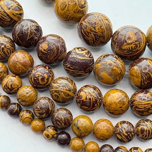 May include: Close-up of various sizes of round beads. The beads have a marbled appearance with a mix of brown and yellow-tan colors. The beads are strung together, suggesting they are for jewelry making or crafts.