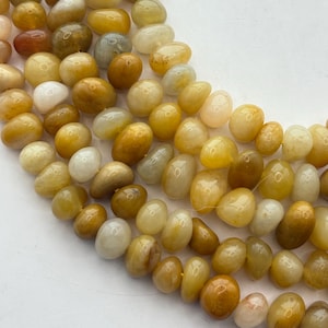 May include: Close-up of strands of yellow-toned gemstone beads. The beads have a smooth, polished surface and vary in color from pale yellow to deep amber. The beads are oval-shaped and appear to be strung together for jewelry making.