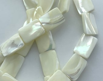 May include: Close-up of a strand of rectangular, iridescent, off-white beads. The beads have a subtle sheen and are strung together, creating a necklace or bracelet. The beads are smooth and have a pearlescent quality.