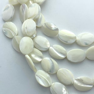 May include: Close-up of a strand of oval-shaped, off-white beads with iridescent, pearlescent surfaces. The beads are arranged in multiple rows, showcasing their smooth texture and subtle color variations. Ideal for jewelry making.