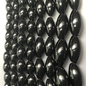 Peut inclure: Gros plan sur plusieurs rang&eacute;es de perles ovales gris fonc&eacute;. Les perles ont une surface brillante et r&eacute;fl&eacute;chissante. Elles sont enfil&eacute;es, probablement pour des projets de bijoux ou d'artisanat. Les perles sont de taille et de forme uniformes.
