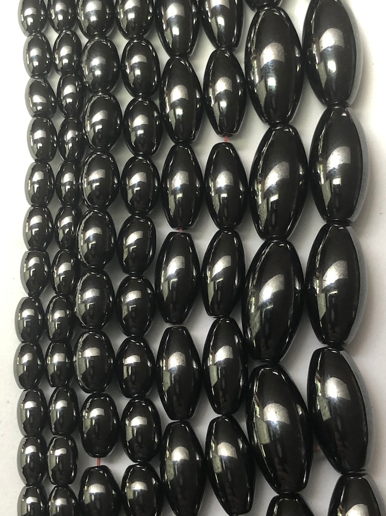 Peut inclure: Gros plan sur plusieurs rang&eacute;es de perles ovales gris fonc&eacute;. Les perles ont une surface brillante et r&eacute;fl&eacute;chissante. Elles sont enfil&eacute;es, probablement pour des projets de bijoux ou d'artisanat. Les perles sont de taille et de forme uniformes.