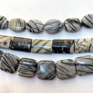 May include: Strands of natural stone beads in various shapes: oval, rectangular, and square. The beads are primarily gray with intricate black veining patterns. The beads are smooth and polished, showcasing the natural stone's beauty.