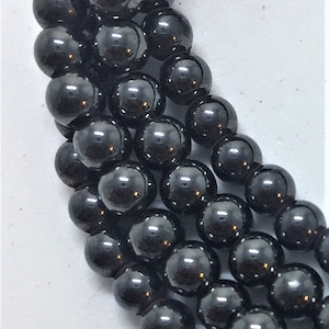 May include: Close-up of strands of black, glossy, round beads. The beads are evenly sized and reflect light, creating a shiny appearance. The beads are likely for jewelry making or crafting.