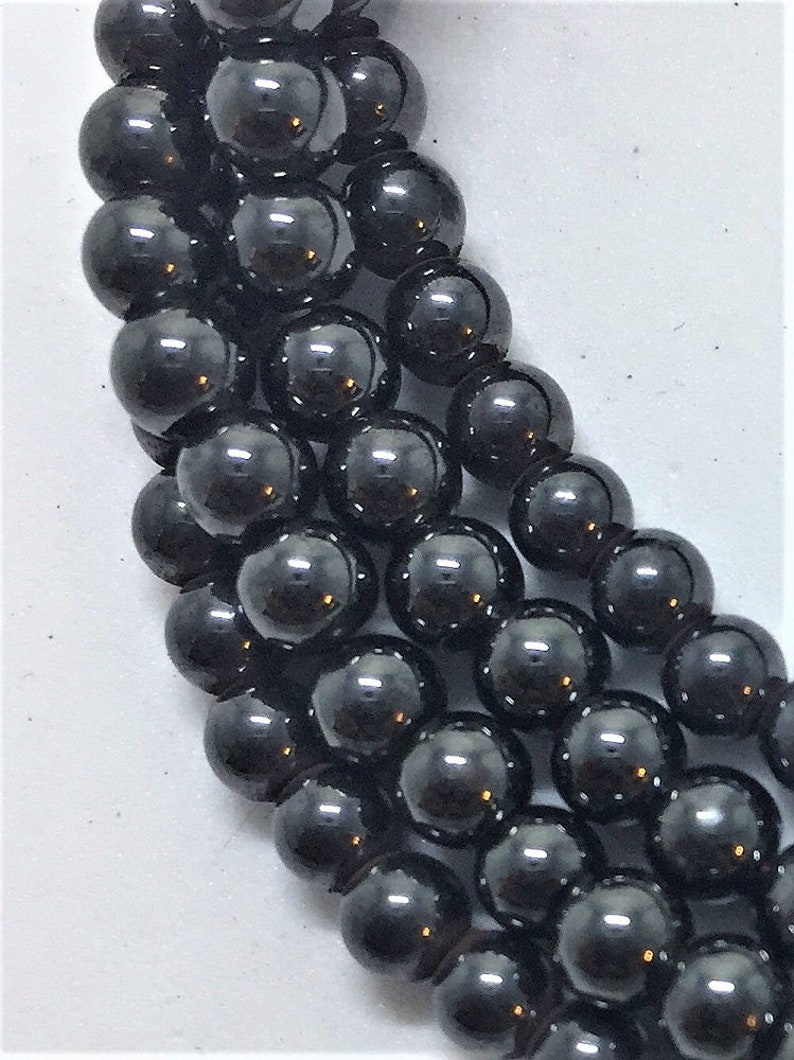May include: Close-up of strands of black, glossy, round beads. The beads are evenly sized and reflect light, creating a shiny appearance. The beads are likely for jewelry making or crafting.