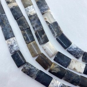 May include: Close-up of strands of rectangular beads in shades of gray, black, and white. The beads have a marbled appearance, with intricate patterns and variations in color. The beads are strung together, creating a necklace or bracelet.