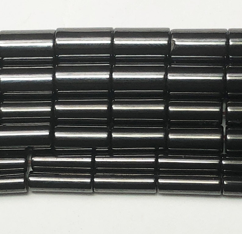 May include: Close-up of a collection of black, cylindrical beads. The beads are arranged in neat rows, each bead reflecting light. The beads appear to be made of a smooth, polished material. The overall effect is a dark, glossy texture.