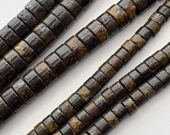 May include: Close-up of several strands of dark brown, cylindrical beads. The beads have a textured, mottled appearance with variations of brown and tan. The beads are strung together, creating a pattern of repeating shapes. The background is a plain white surface.