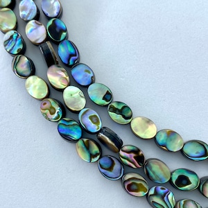 May include: Three strands of iridescent oval-shaped beads. The beads display a range of colors, including blues, greens, and yellows, with a shimmering, pearlescent effect. The beads are strung together, suggesting they are for jewelry making.