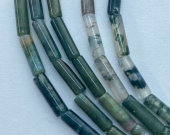 May include: Strands of cylindrical beads in shades of green, gray, and white. The beads have a polished finish and vary in color, with some showing a moss-like pattern. The beads are strung together, creating a flowing, organic look, suitable for jewelry making.