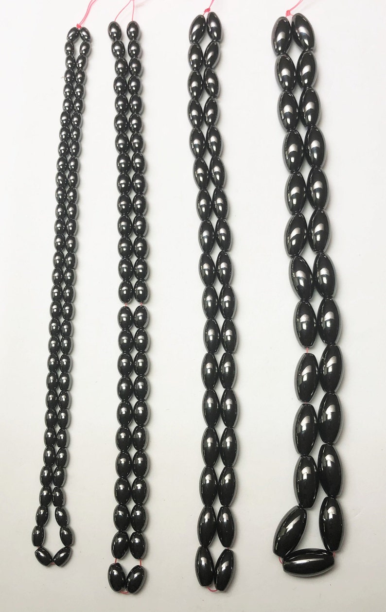 Peut inclure: Quatre rang&eacute;es de perles sombres et brillantes, de forme ovale, sont pr&eacute;sent&eacute;es sur fond blanc. Les perles sont enfil&eacute;es sur un fil rouge, avec des arrangements vari&eacute;s. Les perles semblent &ecirc;tre faites d'un mat&eacute;riau lisse et r&eacute;fl&eacute;chissant.