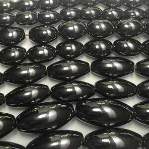 Peut inclure: Gros plan sur des rang&eacute;es de perles noires ovales et brillantes. Les perles sont enfil&eacute;es, peut-&ecirc;tre pour la fabrication de bijoux. Chaque perle a une surface lisse et r&eacute;fl&eacute;chissante. Les perles mesurent environ 1,5 cm de long.