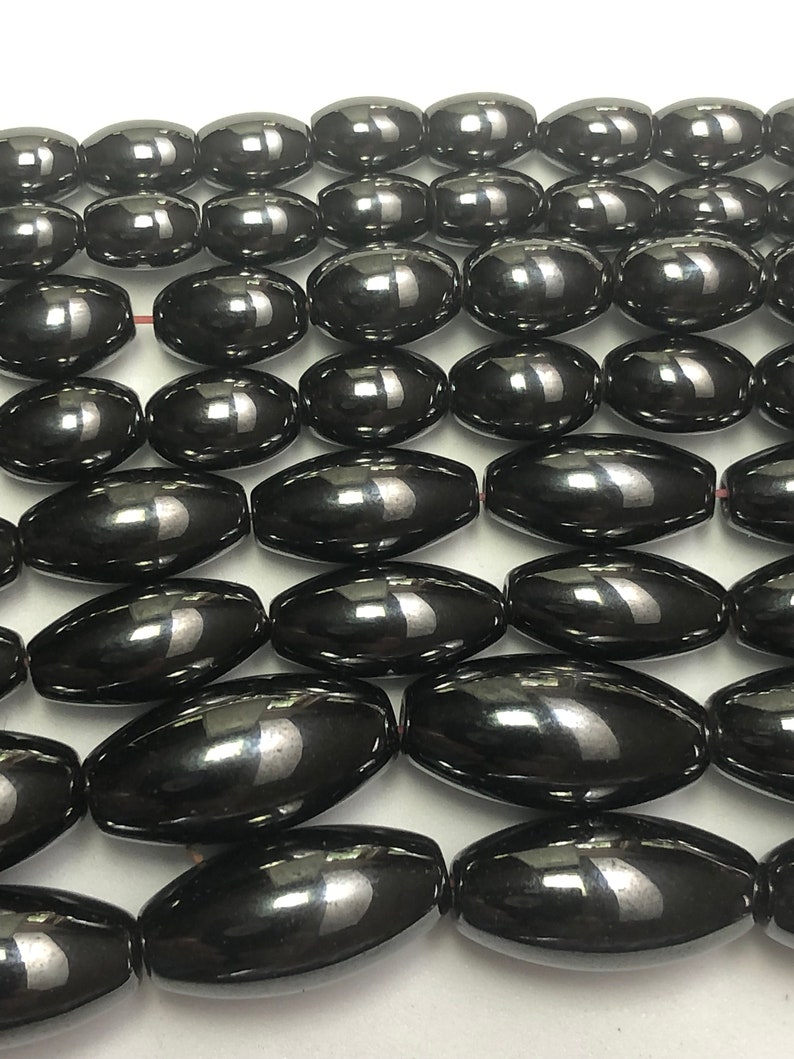 Peut inclure: Gros plan sur des rang&eacute;es de perles noires ovales et brillantes. Les perles sont enfil&eacute;es, peut-&ecirc;tre pour la fabrication de bijoux. Chaque perle a une surface lisse et r&eacute;fl&eacute;chissante. Les perles mesurent environ 1,5 cm de long.