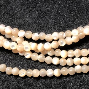 May include: Close-up of several strands of lustrous, round, peach-colored beads. The beads have a subtle iridescence, reflecting light. The strands are arranged in a layered pattern, creating a sense of depth. These beads are suitable for jewelry making.