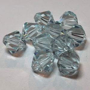 May include: A collection of faceted, light blue crystal beads. The beads have multiple facets that reflect light, creating a sparkling effect. The beads are clustered together, suggesting they are for jewelry making or crafting.