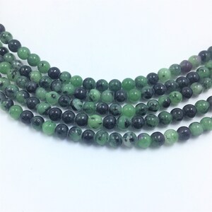 May include: Strands of round beads in shades of green and black. The beads have a polished, glossy finish and are strung together, creating a necklace or bracelet component. The beads are a natural stone material.