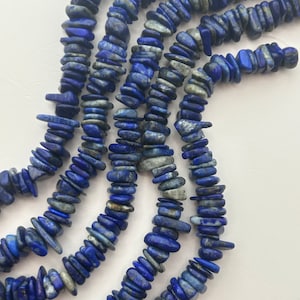 May include: Strands of lapis lazuli gemstone beads in varying shades of blue and gray. The beads are irregularly shaped, creating a natural, organic look. These beads are suitable for jewelry making.