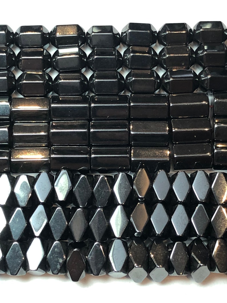 May include: Close-up of several strands of black gemstone beads. The beads are in various shapes, including faceted rectangles, cylinders, and diamond shapes. The beads have a glossy, reflective surface, and are strung together. The background is white.
