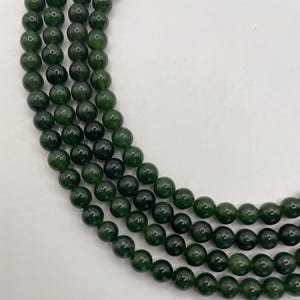 May include: Strands of dark green, round beads. The beads have a polished, glossy finish and are strung together, creating a layered effect. The beads are a deep, forest green color, and the image is set against a white background.