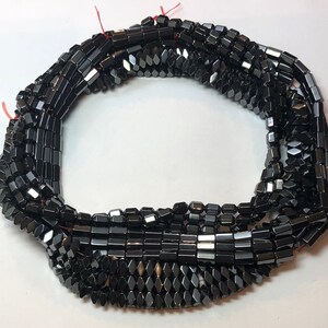 May include: Strands of black, faceted hematite beads. The beads are rectangular and diamond-shaped, strung together with red thread. The beads have a polished, reflective surface, and are suitable for jewelry making.