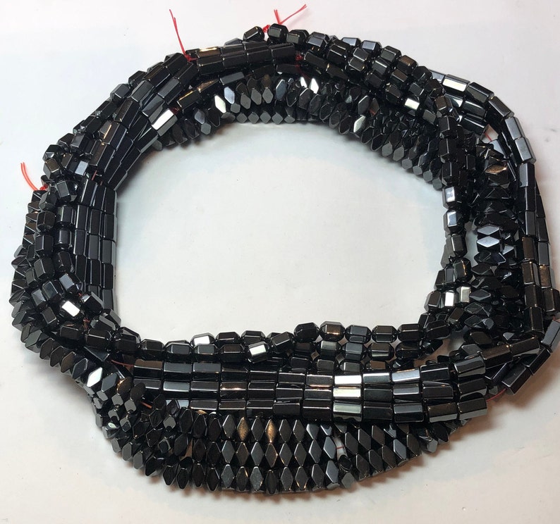 May include: Strands of black, faceted hematite beads. The beads are rectangular and diamond-shaped, strung together with red thread. The beads have a polished, reflective surface, and are suitable for jewelry making.