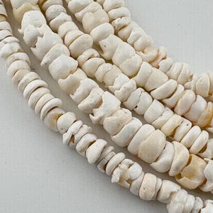 May include: Four strands of off-white, irregularly shaped, disc-like beads arranged in a parallel, curved formation. The beads have a matte, porous texture with subtle variations in tone, ranging from bright white to pale cream and light tan.