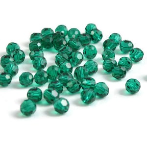 May include: A collection of faceted, emerald green beads scattered on a white surface. The beads are round with multiple facets, creating a sparkling effect. Ideal for jewelry making or craft projects.