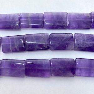 May include: Close-up of a strand of rectangular amethyst beads. The beads are a deep purple color with lighter purple and white inclusions. The beads are smooth and polished, and appear to be strung together.